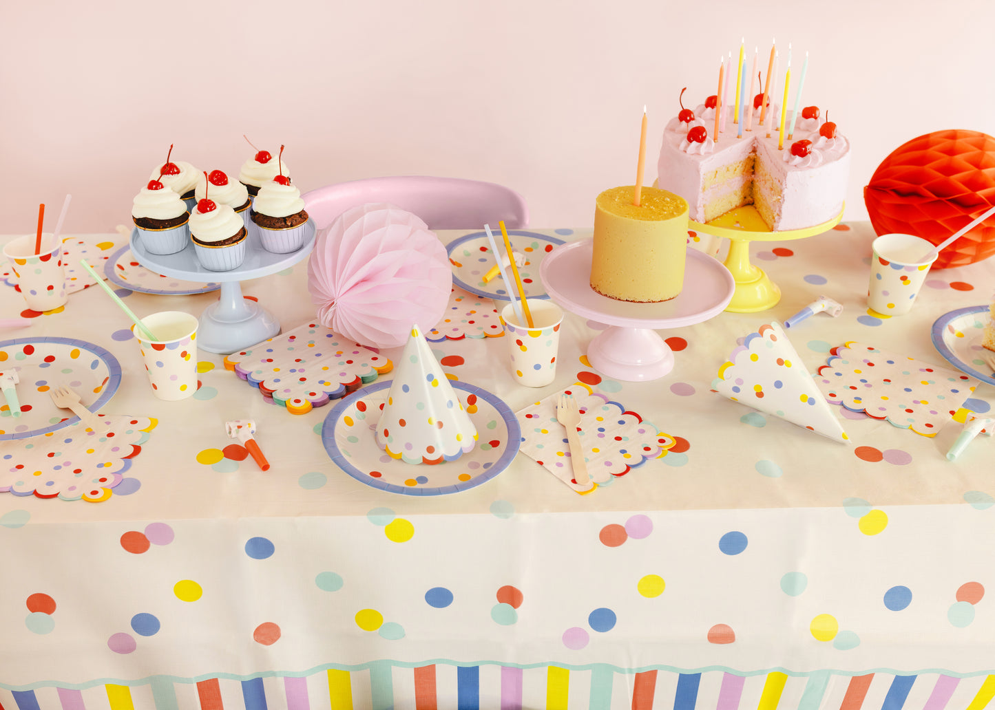 Party table setting with colorful polka dot tablecloth, plates, cups, and decorations.