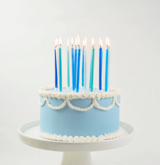 Light blue cake with white frosting and blue candles on a white background