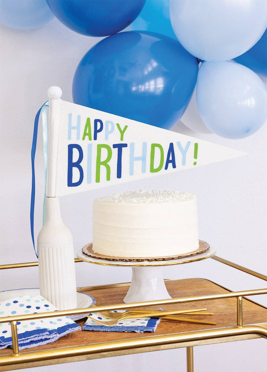 Happy Birthday felt pennant banner displayed with birthday cake with blue balloons and party table decor, available at our Toronto party shop.