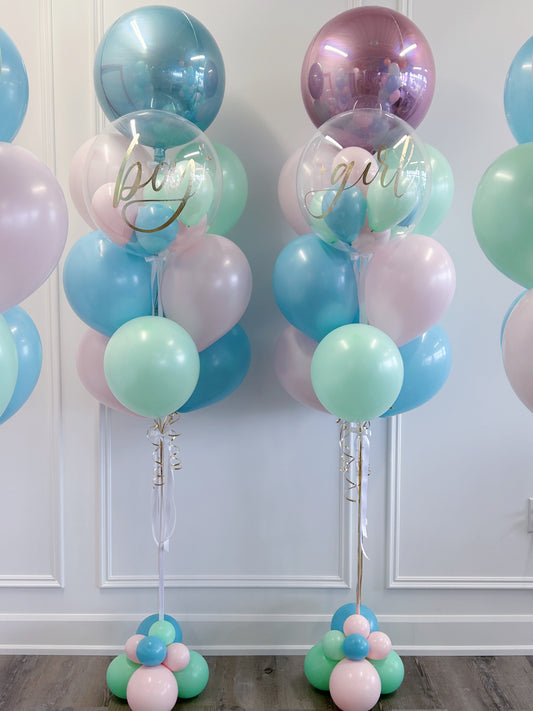 Two balloon bouquet stands decorated with pastel pink, light blue, mint green, and metallic lavender balloons, including a large clear round balloon with gold script text reading 'big girl'.