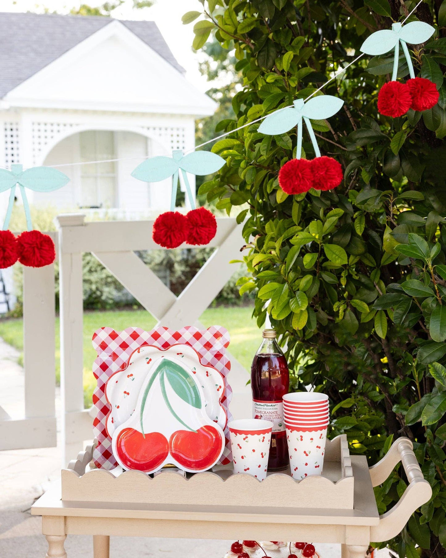 Cherry pom pom felt banner hanging as party décor on a patio table setup, sold in Toronto at Confetti My Party