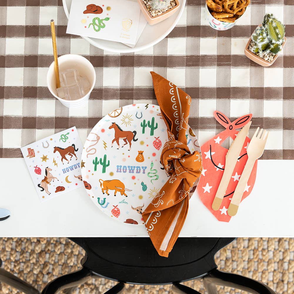 Cowboy party table decor featuring horseshoe napkins, western tableware, and themed place settings.