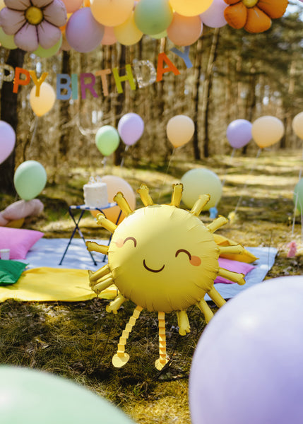Outdoor birthday celebration with balloons and a sun-shaped balloon in a forest setting.