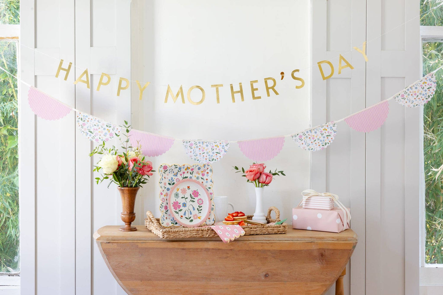 Decorative setup with 'Happy Mother's Day' banner, flowers, and a wooden table.
