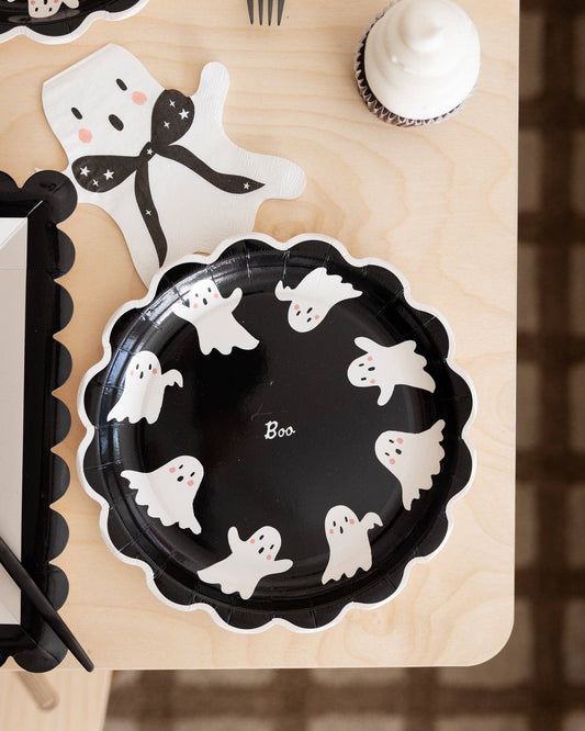 Black paper plate with white ghost designs and 'Boo' text on a wooden surface.