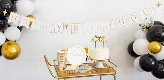 Gold Happy Birthday cake topper displayed on a birthday cake with black, white, and gold party decorations, available at our Toronto party shop.