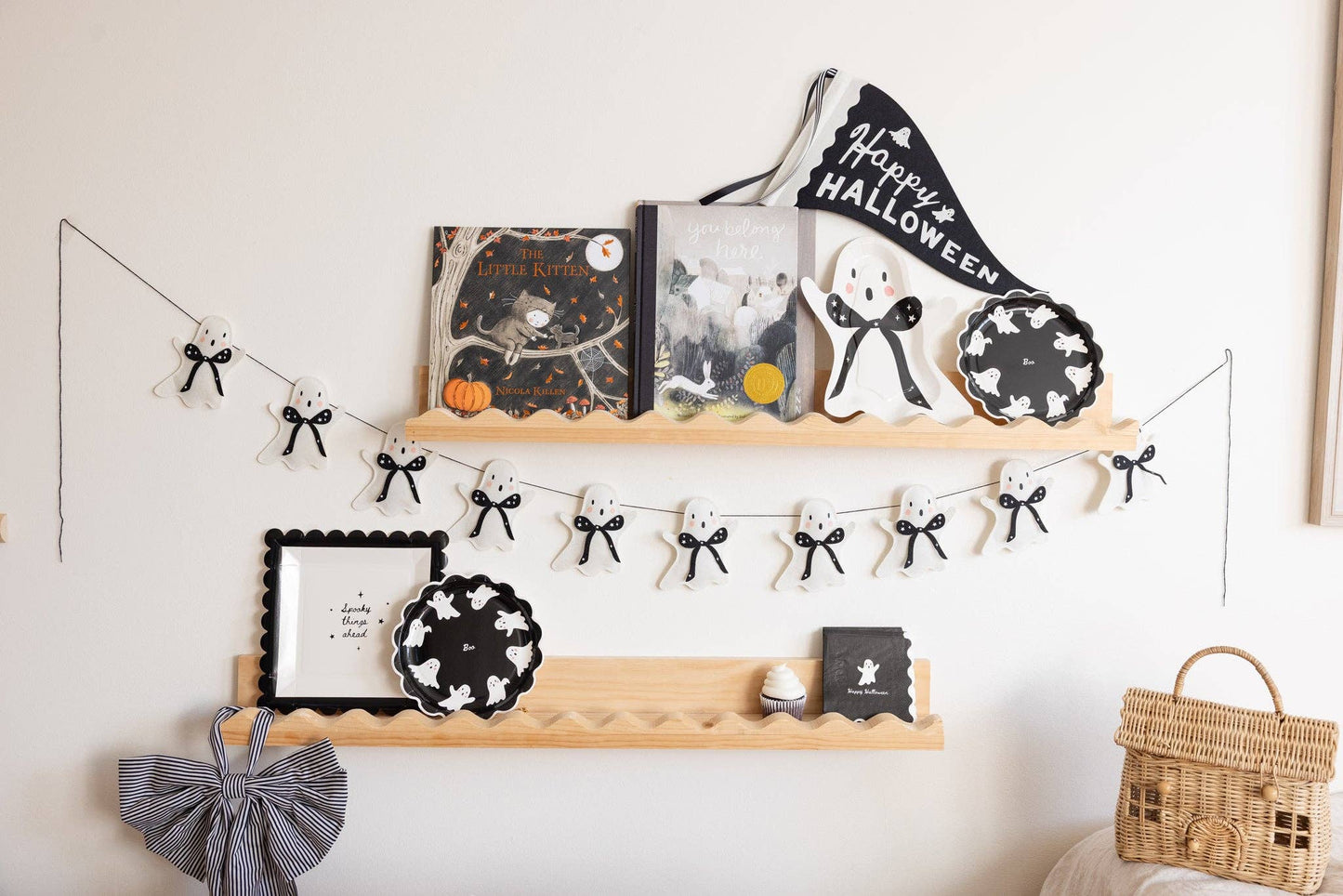 Decorative shelf with Halloween-themed items including books, plates, and a banner on a white wall.