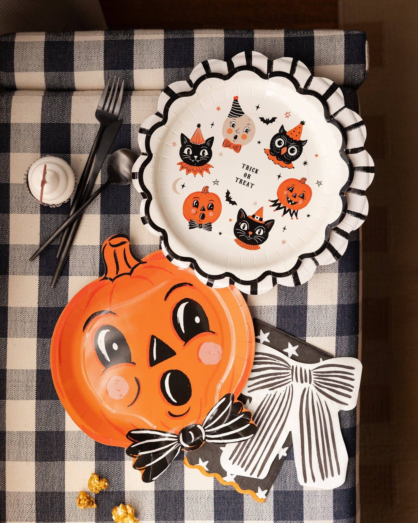 Halloween-themed plates with pumpkins, cats, and ghosts on a checkered tablecloth.
