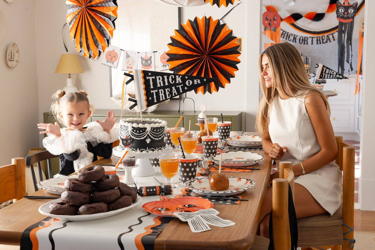 Woman and child at a Halloween-themed table with decorations and treats.