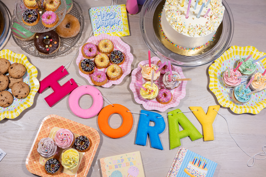 Birthday celebration with cake, donuts, cookies, and colorful 'Hooray' letters on a table.