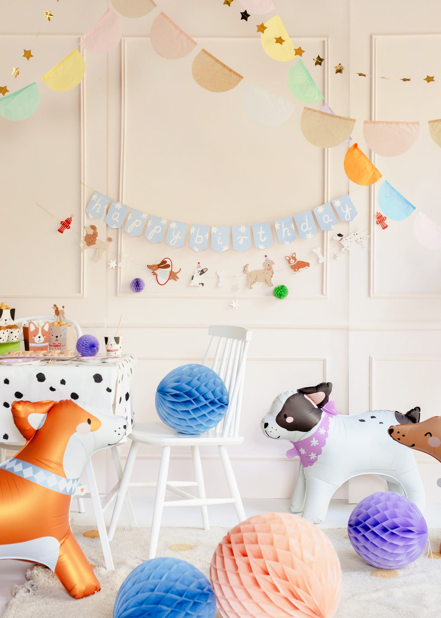 Dog-themed birthday party setup featuring a “happy birthday” banner with illustrated puppies, inflatable dog balloons, honeycomb decorations, and a spotted tablecloth — perfect for a kids’ puppy party or pet-themed celebration.