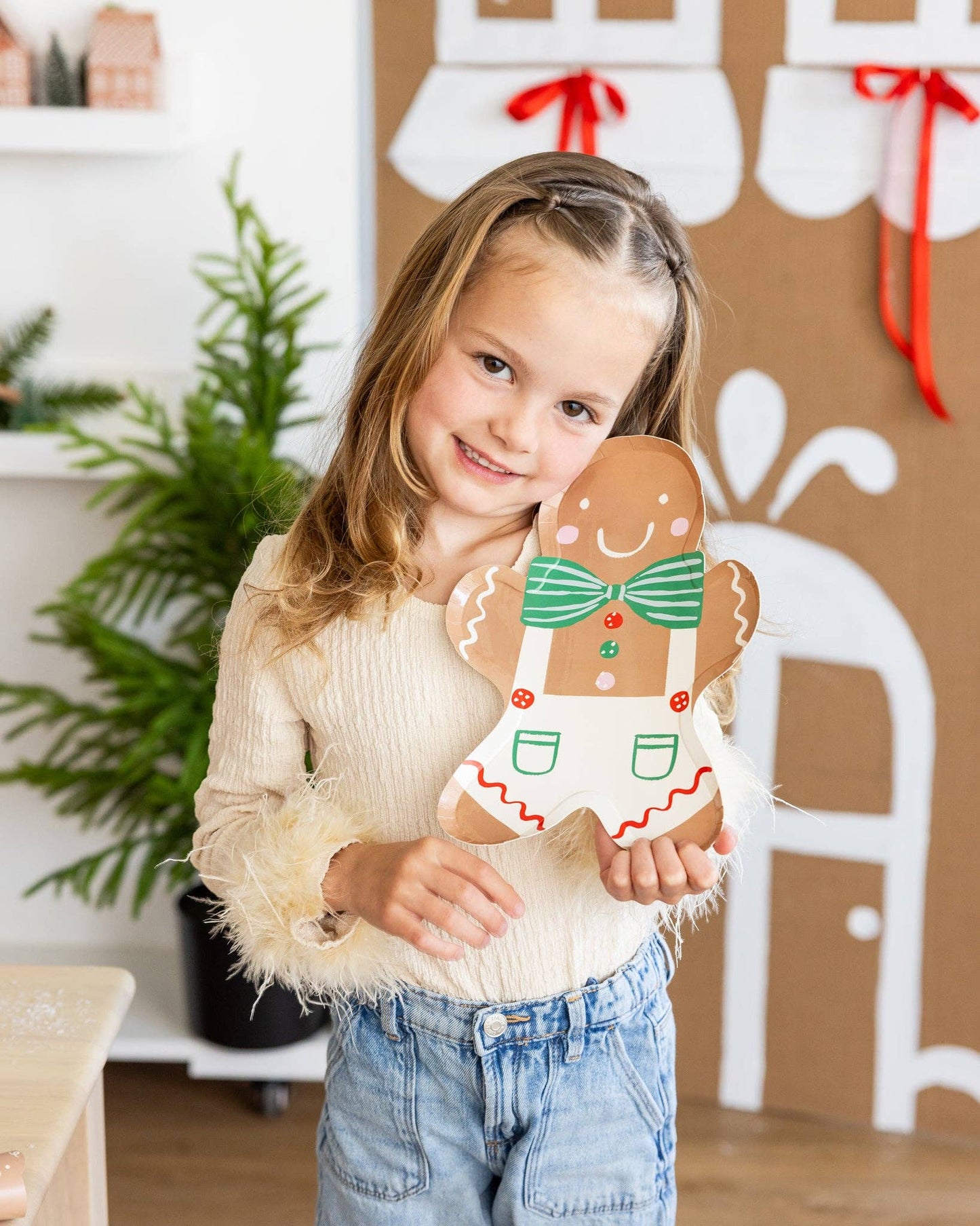 Young girl holding a gingerbread man cookie plate in a festive setting.