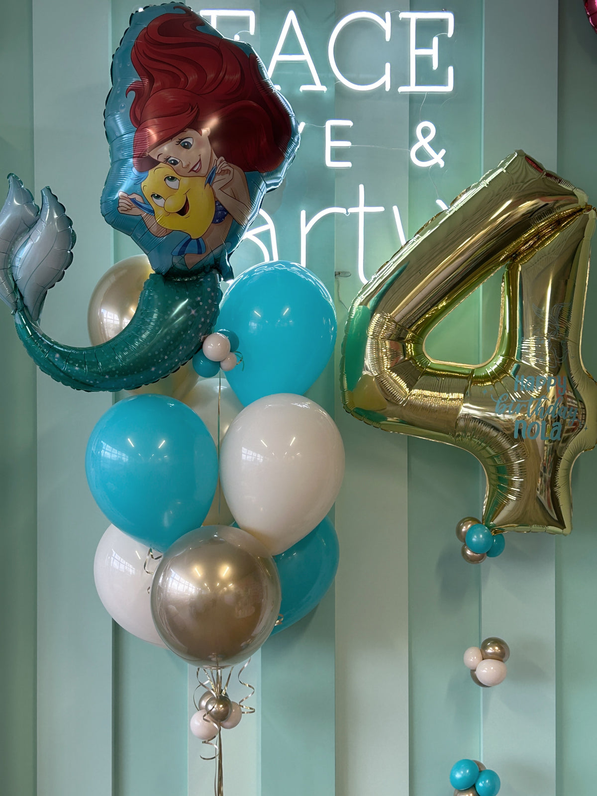 Close-up of Little Mermaid Ariel foil balloon beside a personalized gold number 4 birthday balloon, with turquoise, white and champagne gold latex balloons.