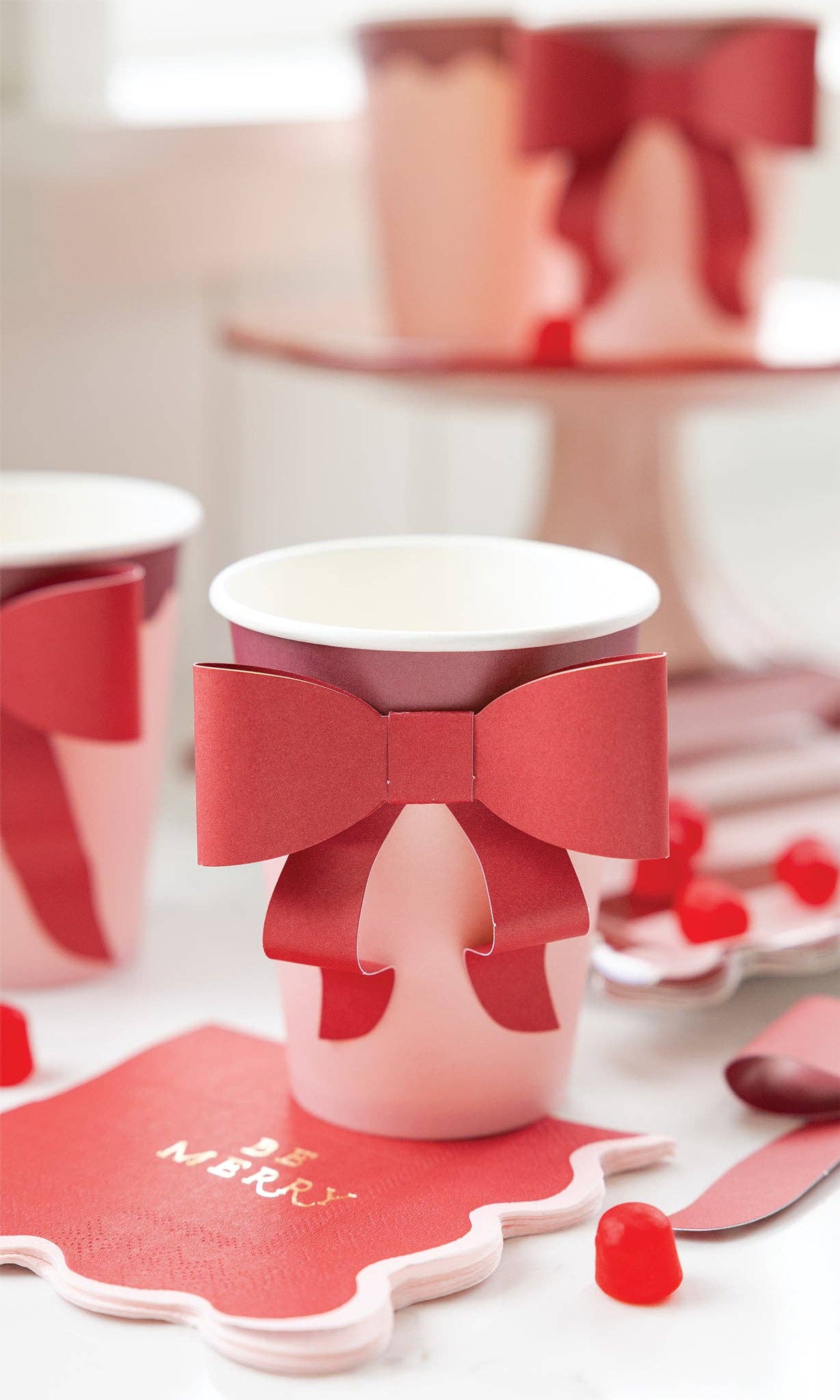 Pink and burgundy bow paper cups styled on holiday dessert table with red accents, Toronto Christmas party décor.