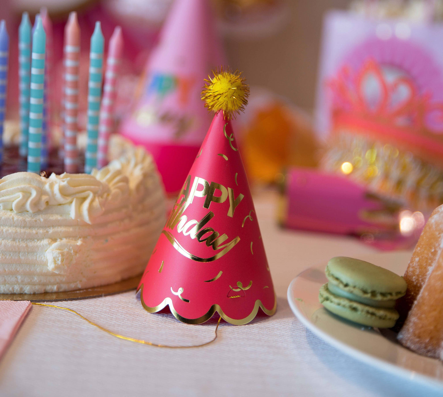 Pink party hat with 'Happy Birthday' text on a table with cake and cookies.