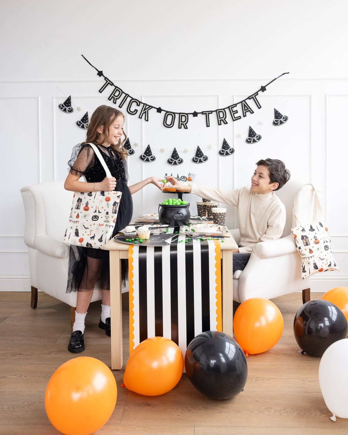 Two children at a Halloween-themed table with balloons and decorations.