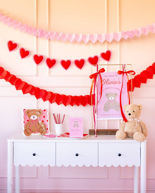 Valentine party table styled with pink and red scalloped paper plates and heart decor