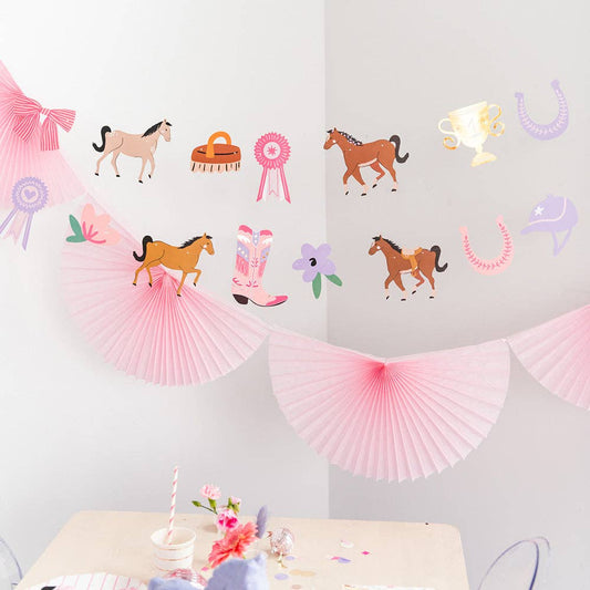 Decorative wall with horse-themed decorations including paper fans, ribbons, and cowboy hats on a light gray background.