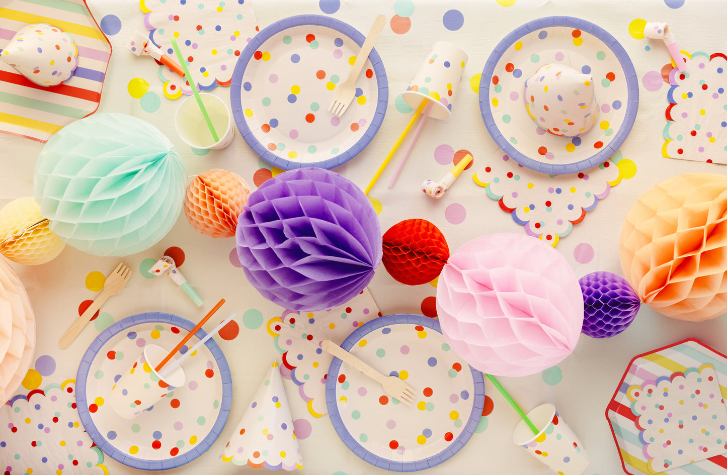 Colorful party supplies including plates, cups, and decorations on a polka dot tablecloth.