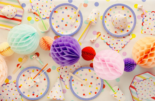 Colorful party supplies including plates, cups, and decorations on a polka dot tablecloth.