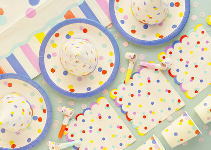 Colorful polka dot partyware including plates, napkins, and cups on a light blue background.