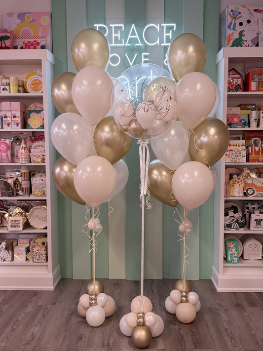Three balloon arrangements featuring champagne gold, pearl white, and cream dusk latex balloons paired with a clear bubble balloon personalized in gold.