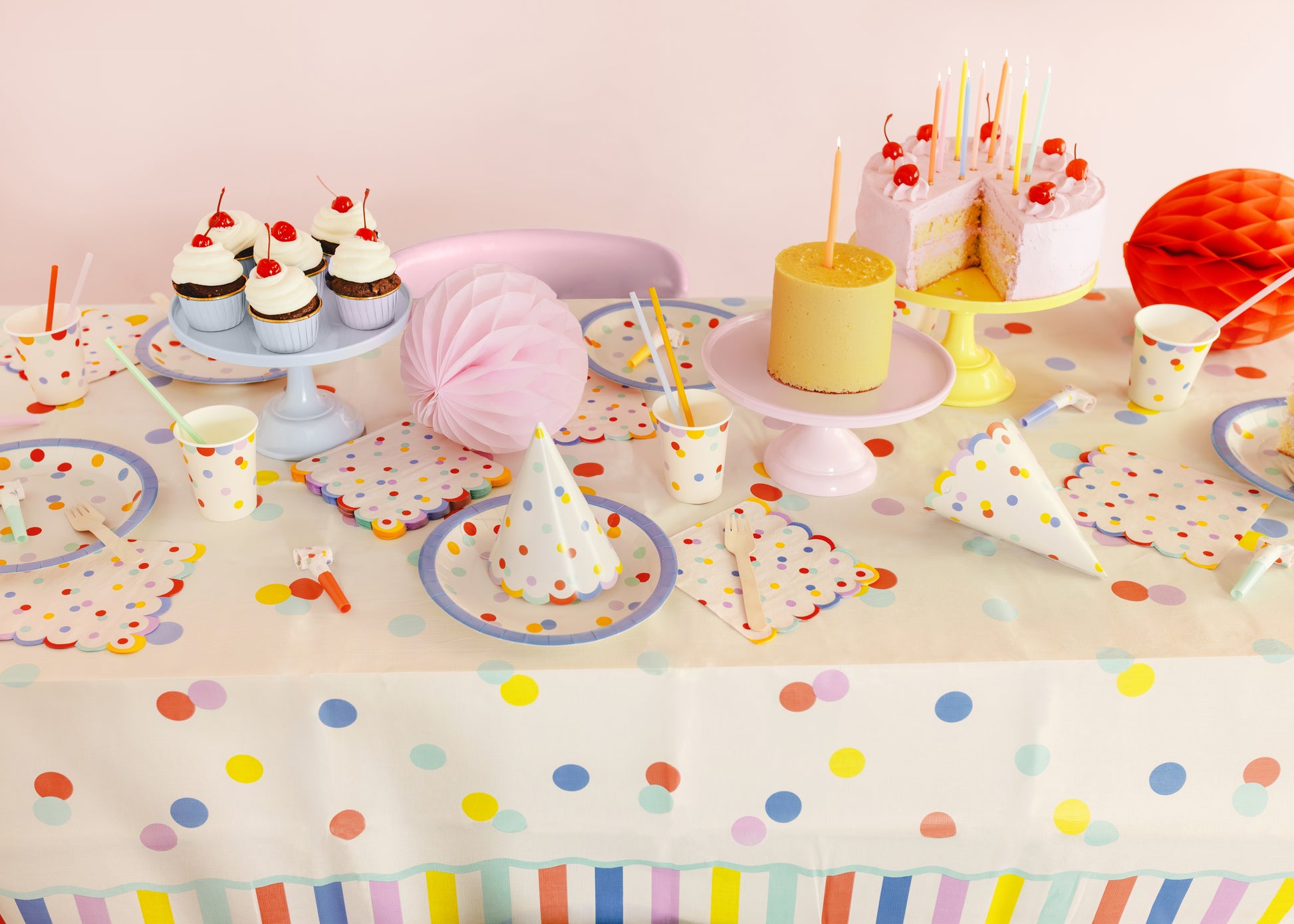Party table setting with colorful polka dot tablecloth, plates, cups, and decorations.