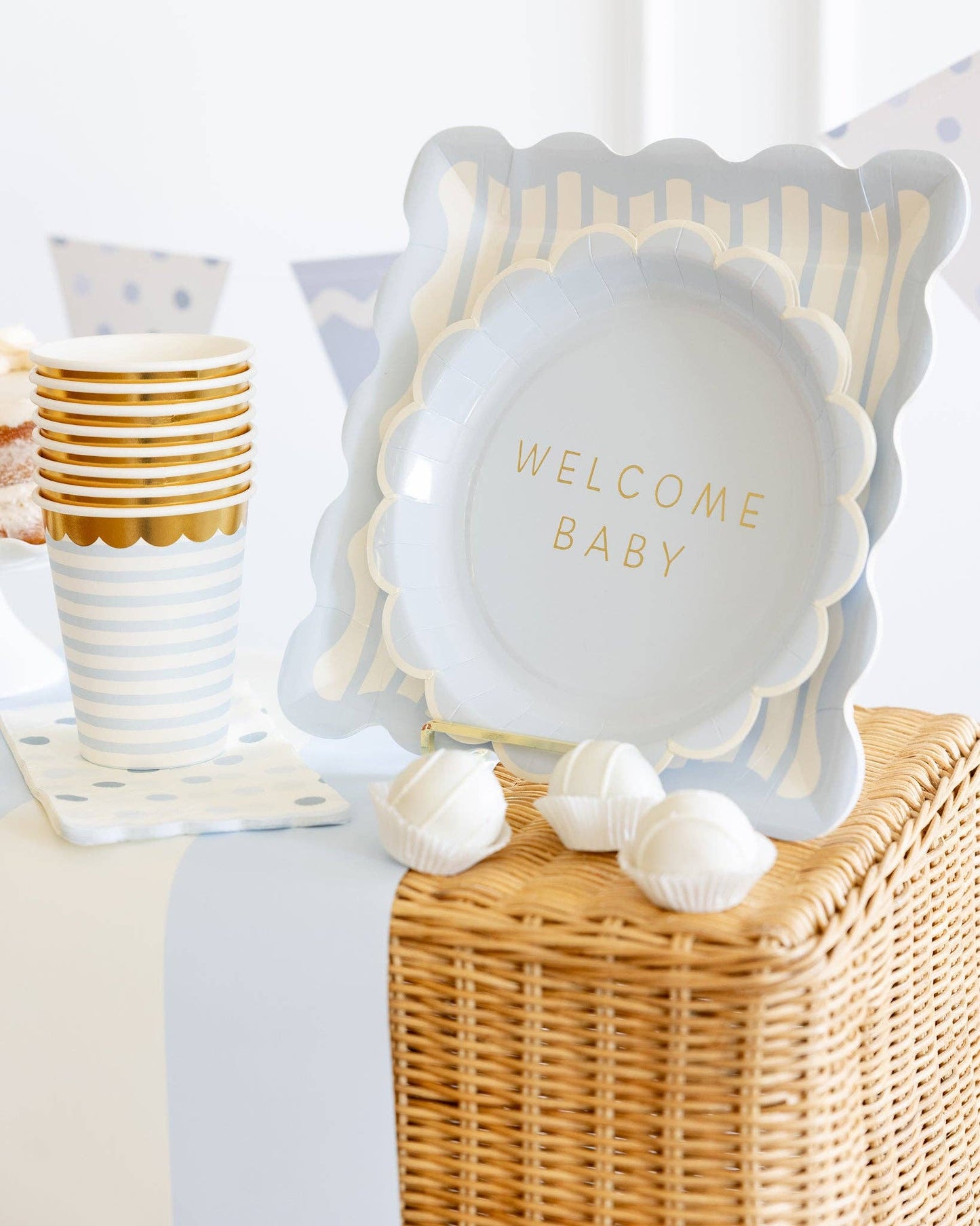 Decorative plate with 'Welcome Baby' text on a wicker box with matching cups.