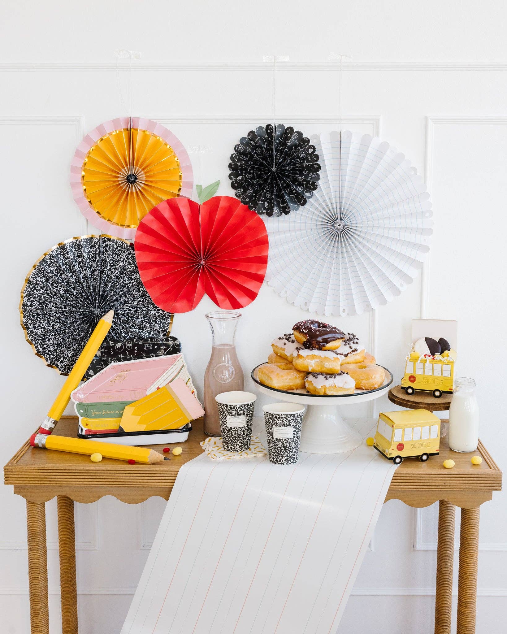 Decorative table with colorful paper fans, donuts, and a cake on a white background
