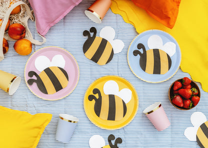 Bee-themed napkins and cups on a striped tablecloth with strawberries.