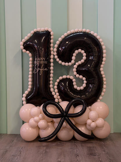 Jumbo black number '13' sitting on a bed of balloons with mini balloon trim accents, personalized for any age.