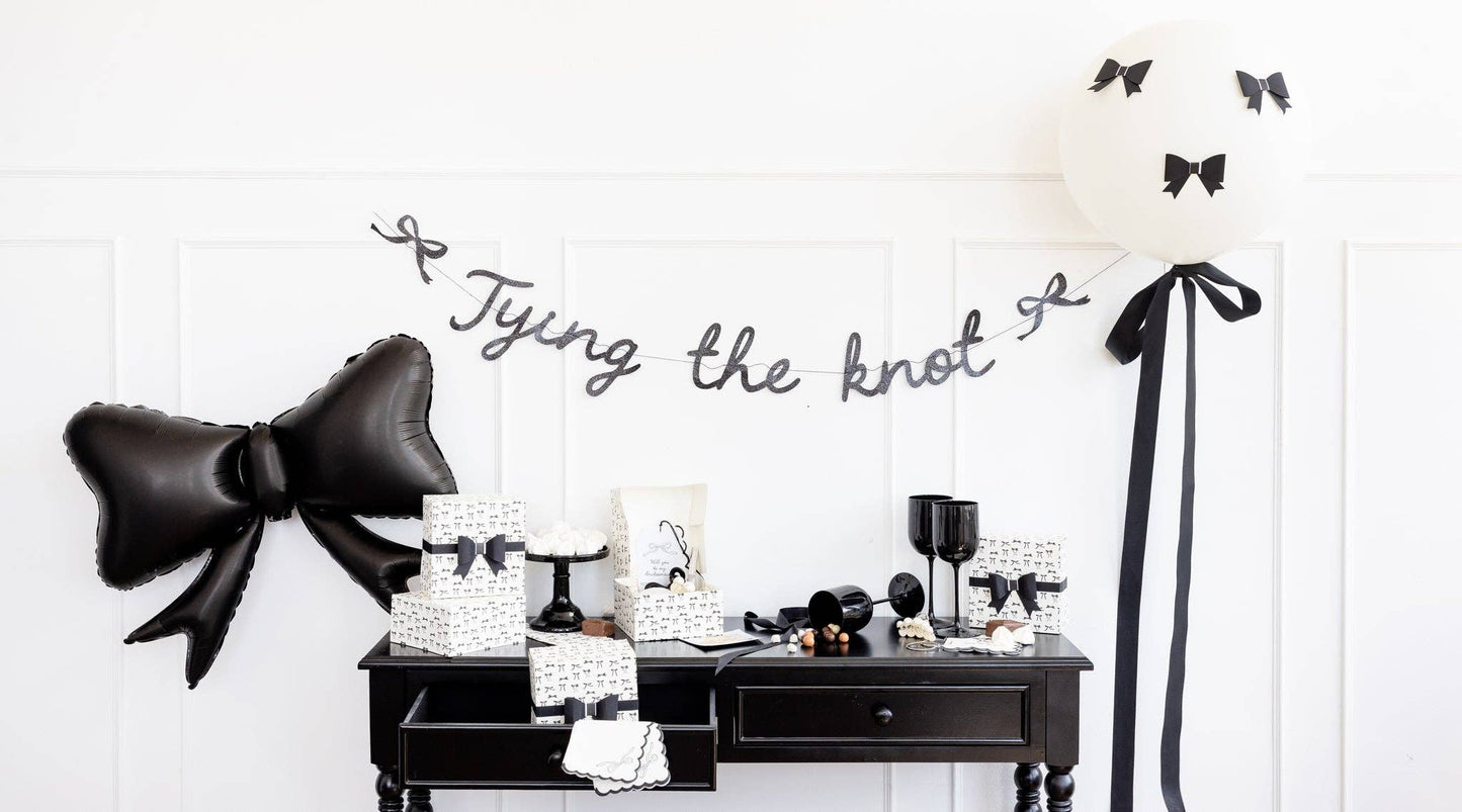 Bridal display featuring black bow guest napkins, Tying the Knot banner, and matching monochrome party décor.