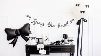 Bridal display featuring black bow guest napkins, Tying the Knot banner, and matching monochrome party décor.