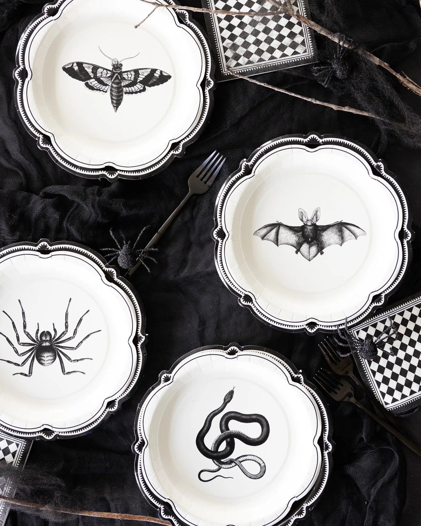 Halloween-themed plates with black spider, bat, and snake designs on a dark surface.
