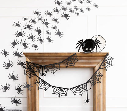 Halloween decorations including spider webs and black spiders on a white wall.