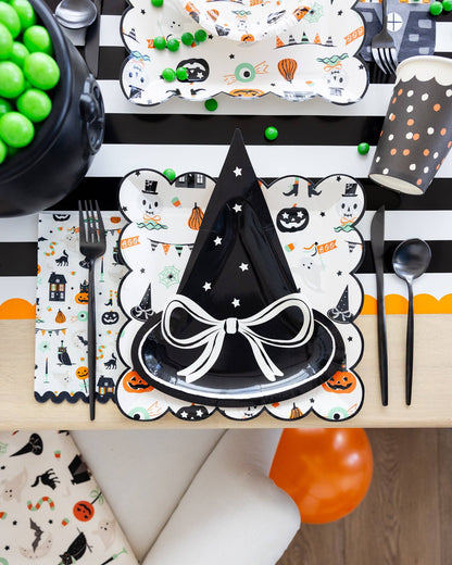 Halloween-themed table setting with witch hat design on placemat, black cutlery, and colorful decorations.