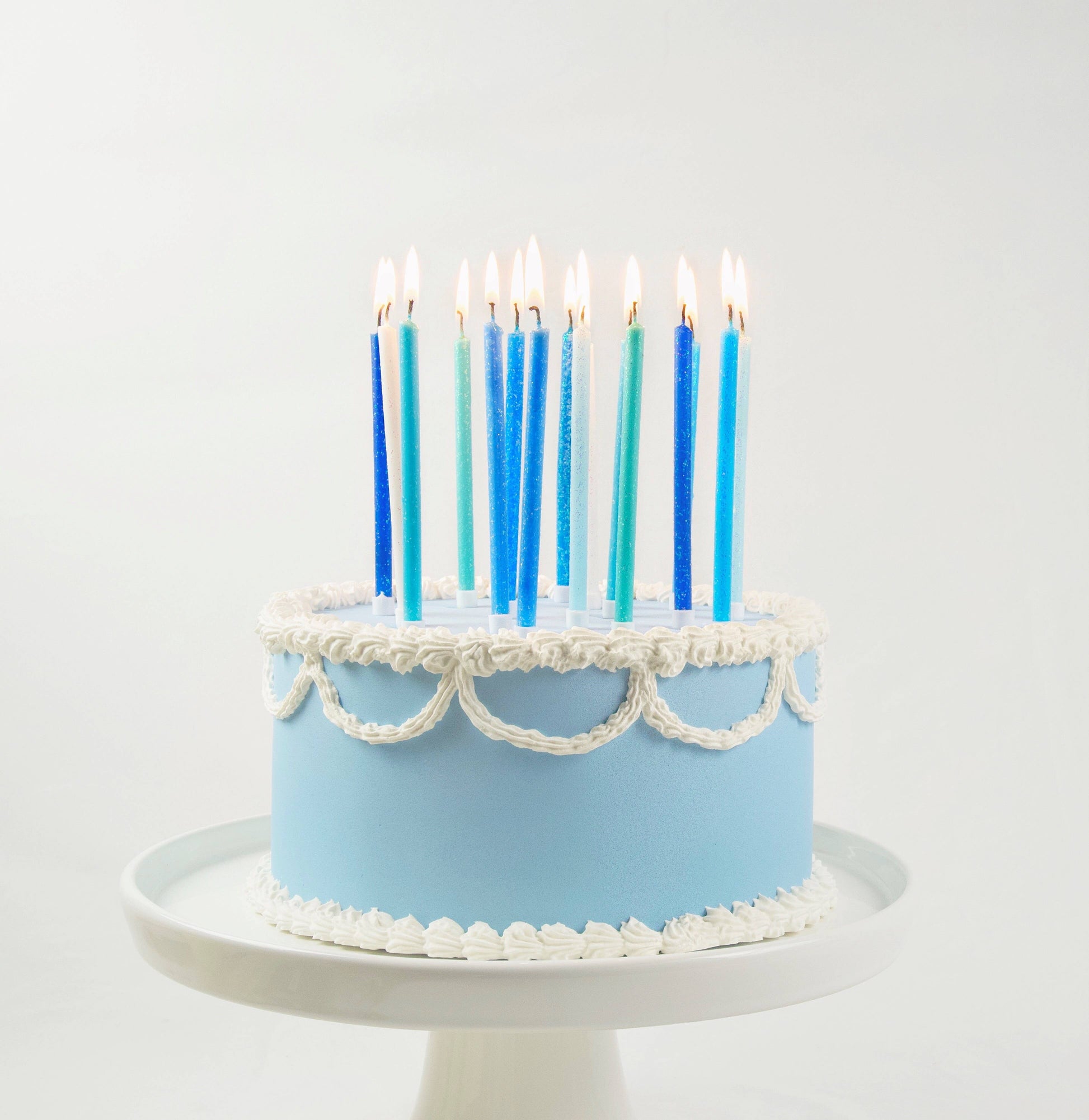 Light blue cake with white frosting and blue candles on a white background