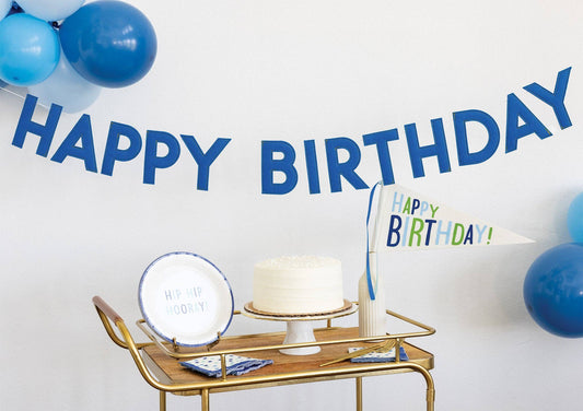 Blue Happy Birthday felt banner displayed above a birthday cake table with balloons, available at our Toronto party shop.