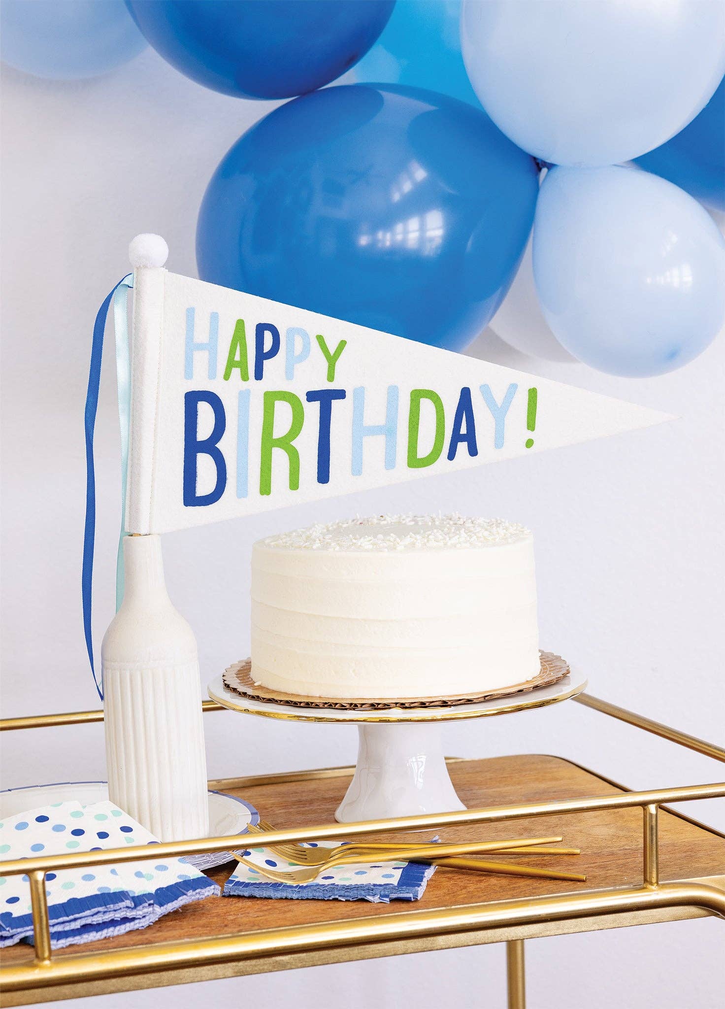 Happy Birthday felt pennant banner displayed with birthday cake with blue balloons and party table decor, available at our Toronto party shop.