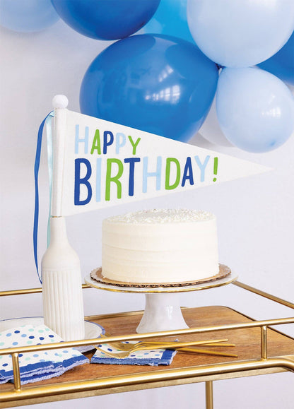 Happy Birthday felt pennant banner displayed with birthday cake with blue balloons and party table decor, available at our Toronto party shop.