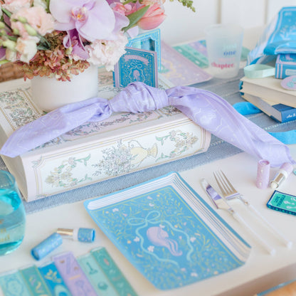 Decorative table setting with books, stationery, and flowers on a white surface.