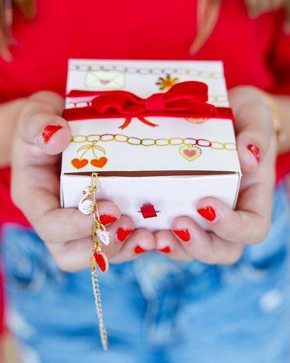 Close-up of a charm bracelet gift box with red bow and gold charms