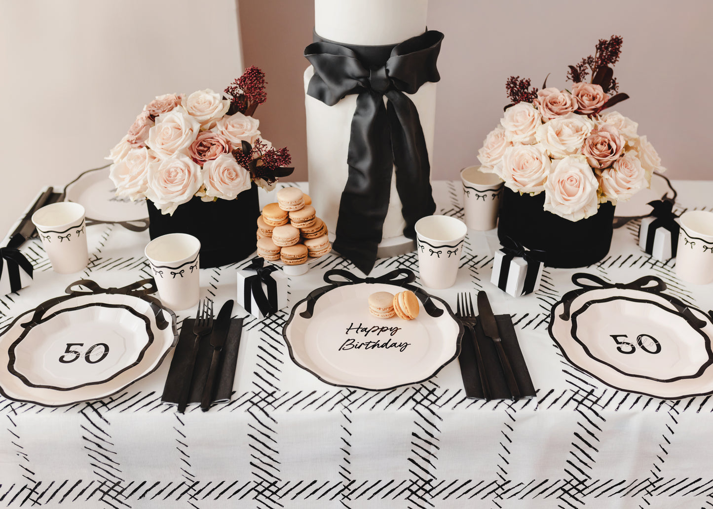 Milestone birthday tablescape with Hello 50 plates, blush flowers, black ribbon cake, and Parisian-inspired party details.