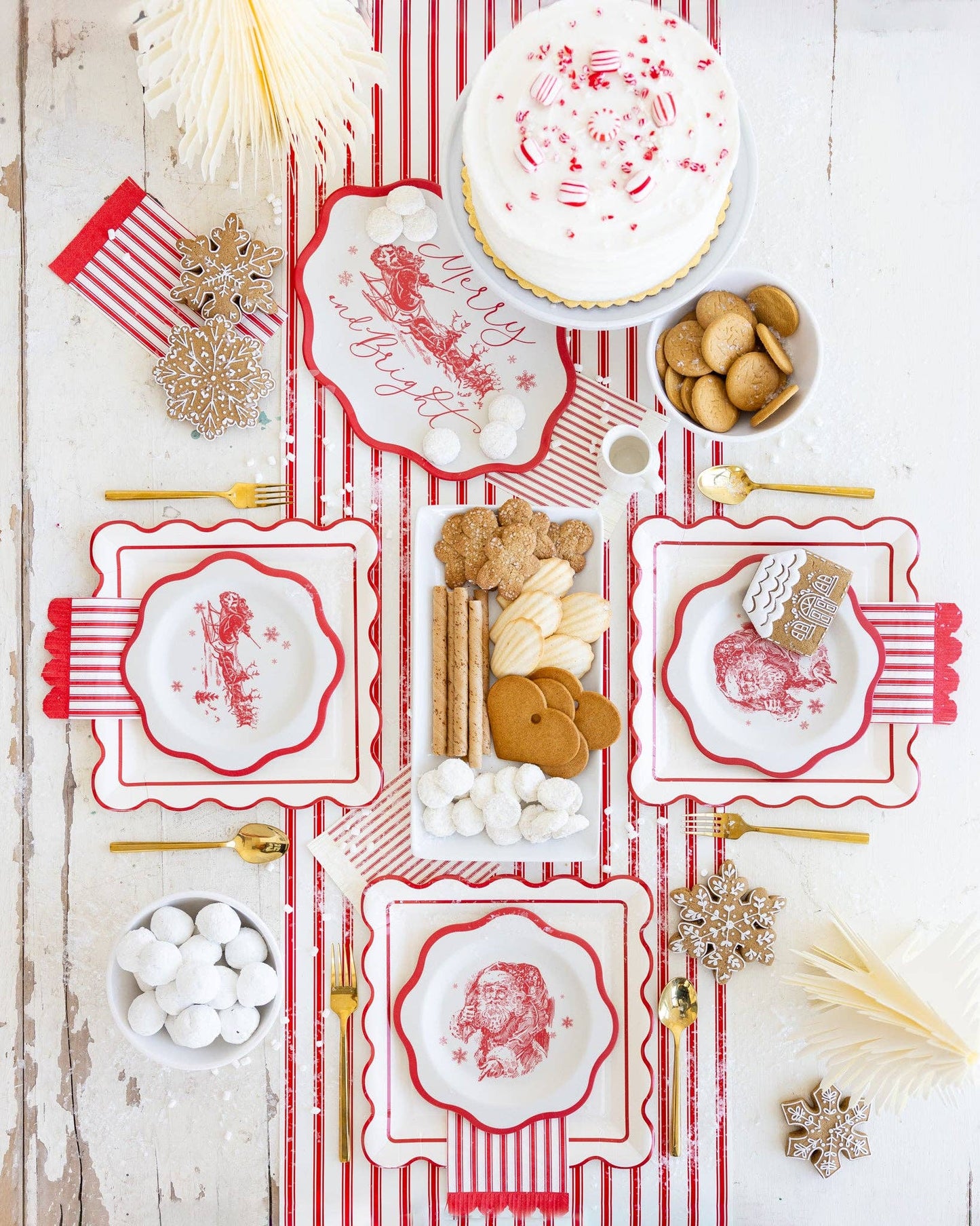 Decorative table setting with red and white patterned plates, cookies, and Christmas decorations on a wooden surface.