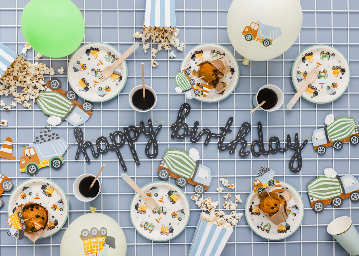 Construction Birthday party setup with plates, cups, and 'happy birthday' sign on a checkered tablecloth.