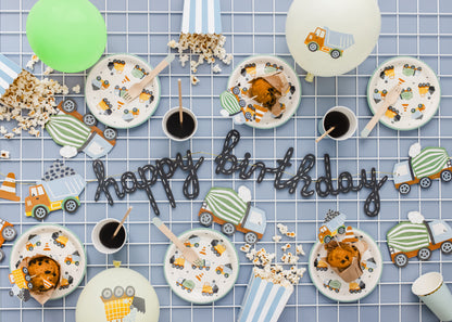 Construction Birthday party setup with plates, cups, and 'happy birthday' sign on a checkered tablecloth.