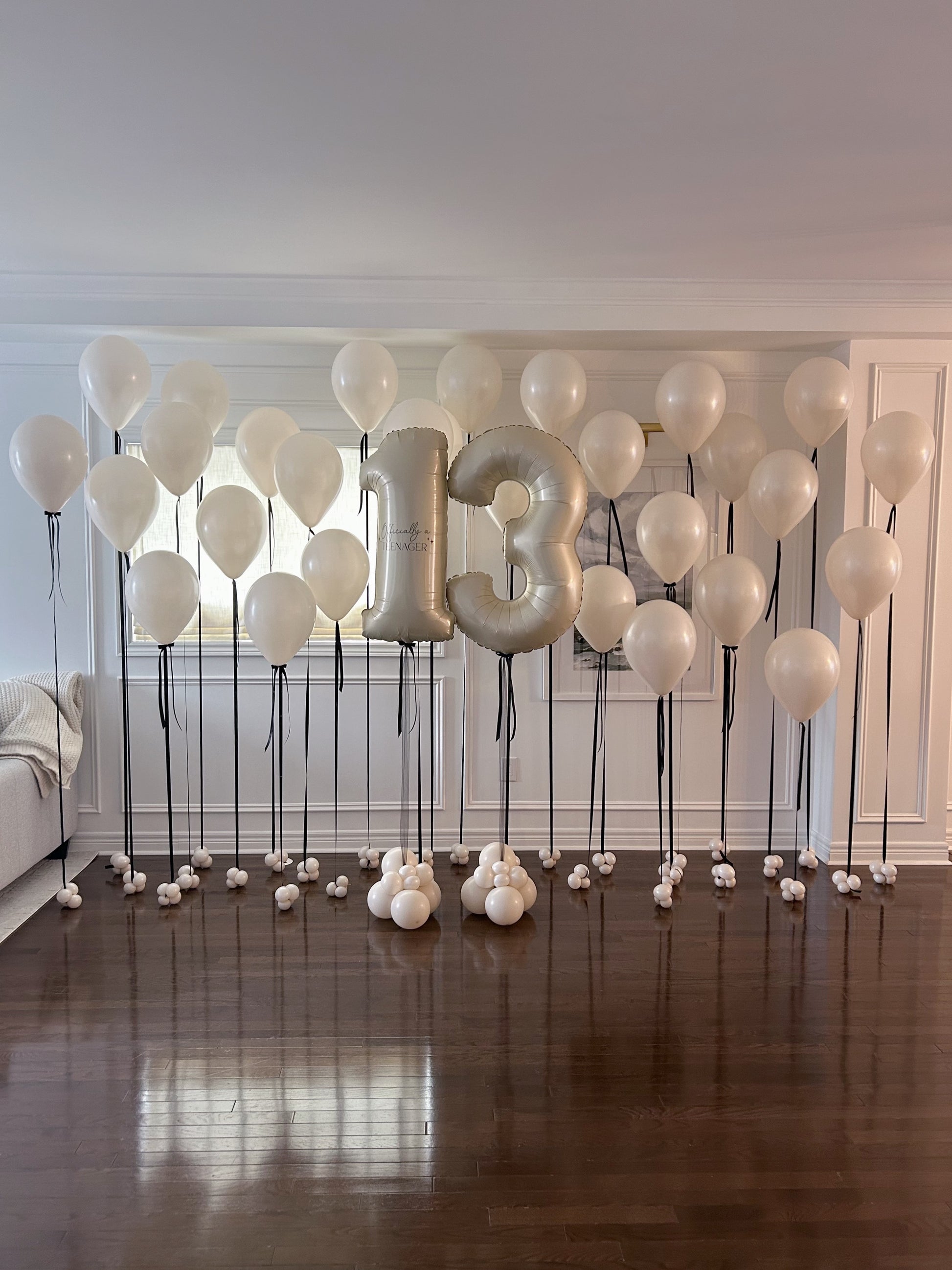Cream helium balloons with black ribbon tails and custom number balloons for a minimalist birthday celebration in Toronto.