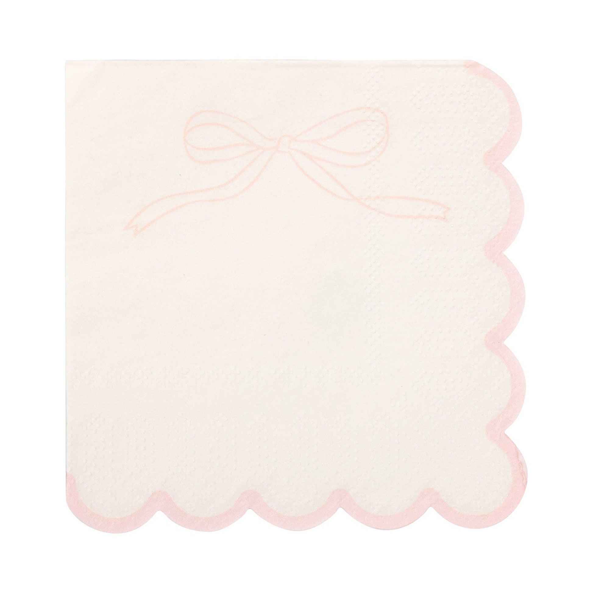 Close-up of a white cocktail napkin featuring a blush pink bow detail and scalloped border.