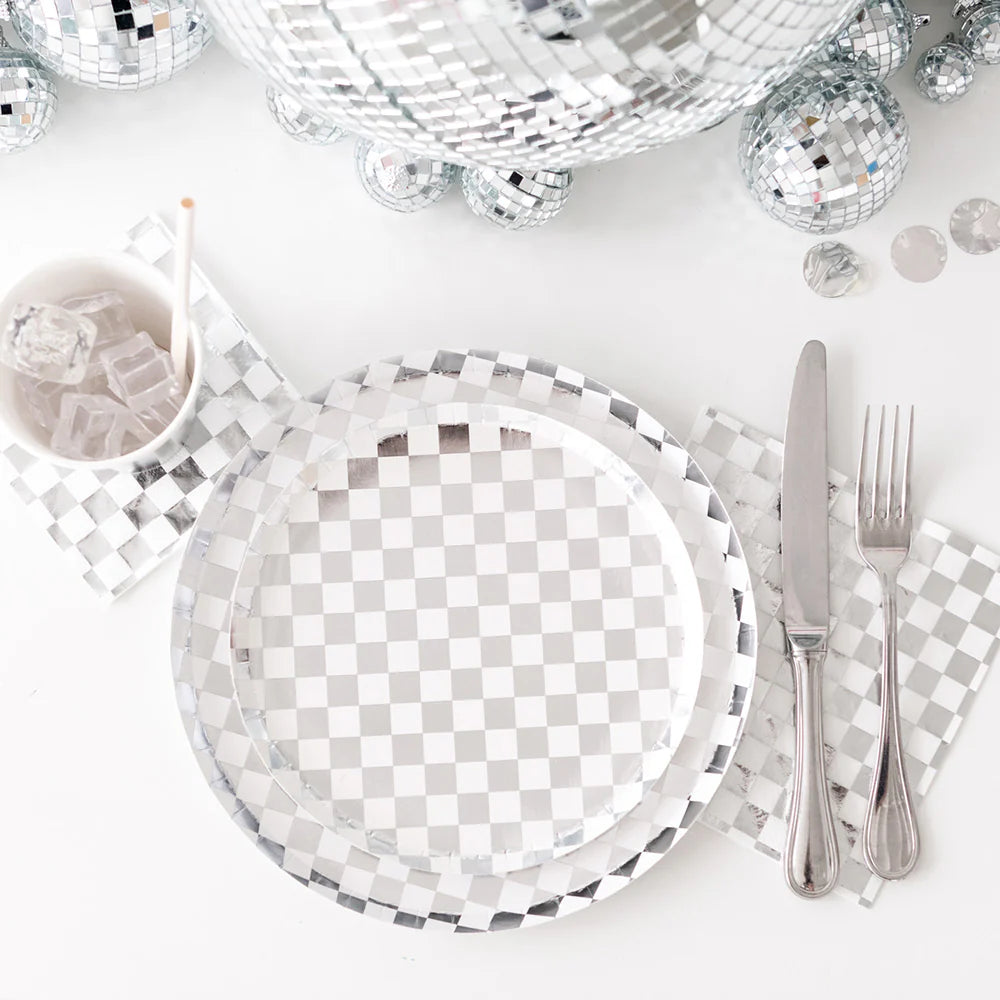Close-up of silver checkered paper plates and napkins styled with clear cutlery and ice-filled cups, surrounded by disco balls. Perfect for a glam party or disco-themed celebration.