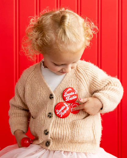 Child in Toronto wearing red Santa buttons and holding elf pennant, festive Christmas photo.